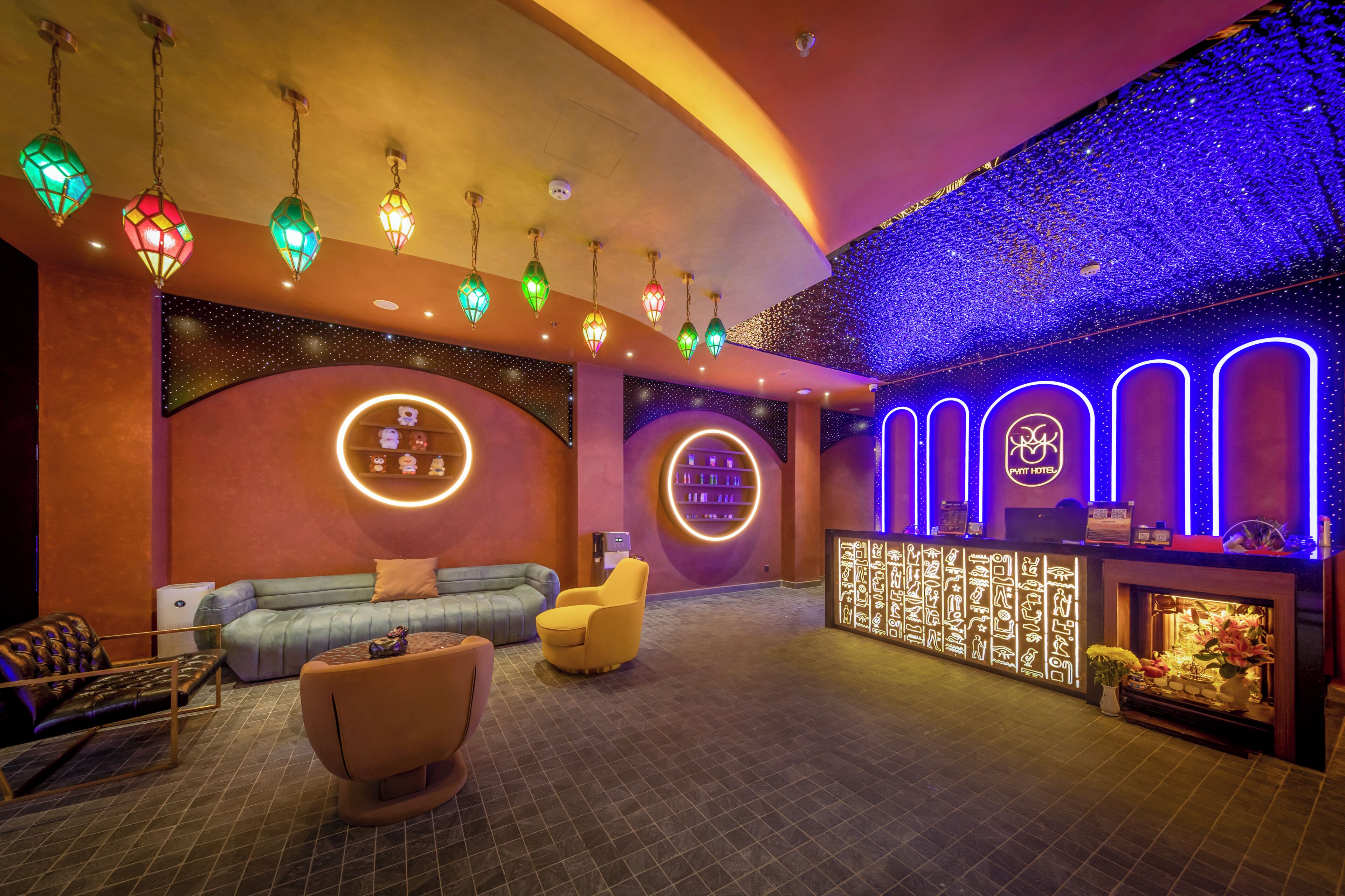 A hotel lobby with a curved ceiling, hanging decorative lights, a reception desk, and a seating area with sofas and chairs.