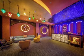Vestíbulo de hotel con techo curvo, luces decorativas colgantes, un mostrador de recepción y un área de descanso con sofás y sillones.