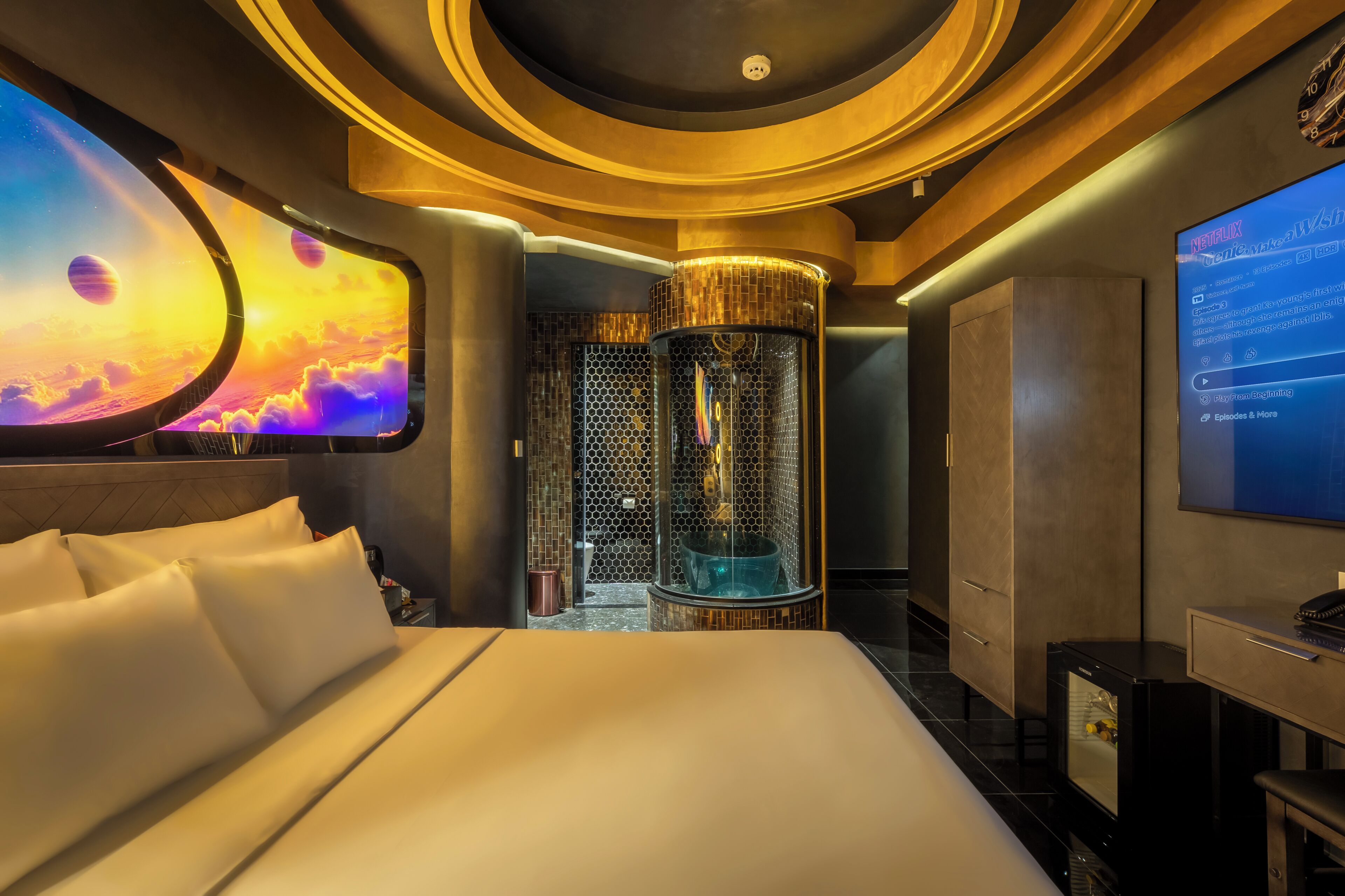 A hotel room with a large bed, a wall-mounted TV, and a unique cylindrical water feature.