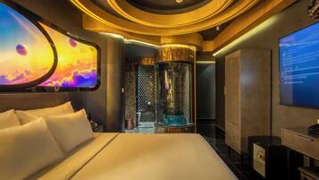 A hotel room with a large bed, a wall-mounted TV, and a unique cylindrical water feature.
