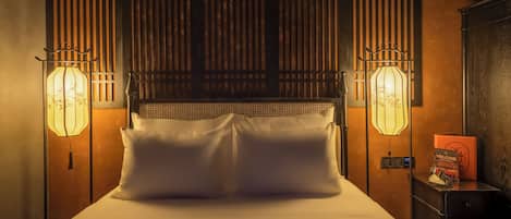 Quarto de hotel com uma cama, duas luminárias na parede, uma mesa de cabeceira e uma cabeceira de madeira.