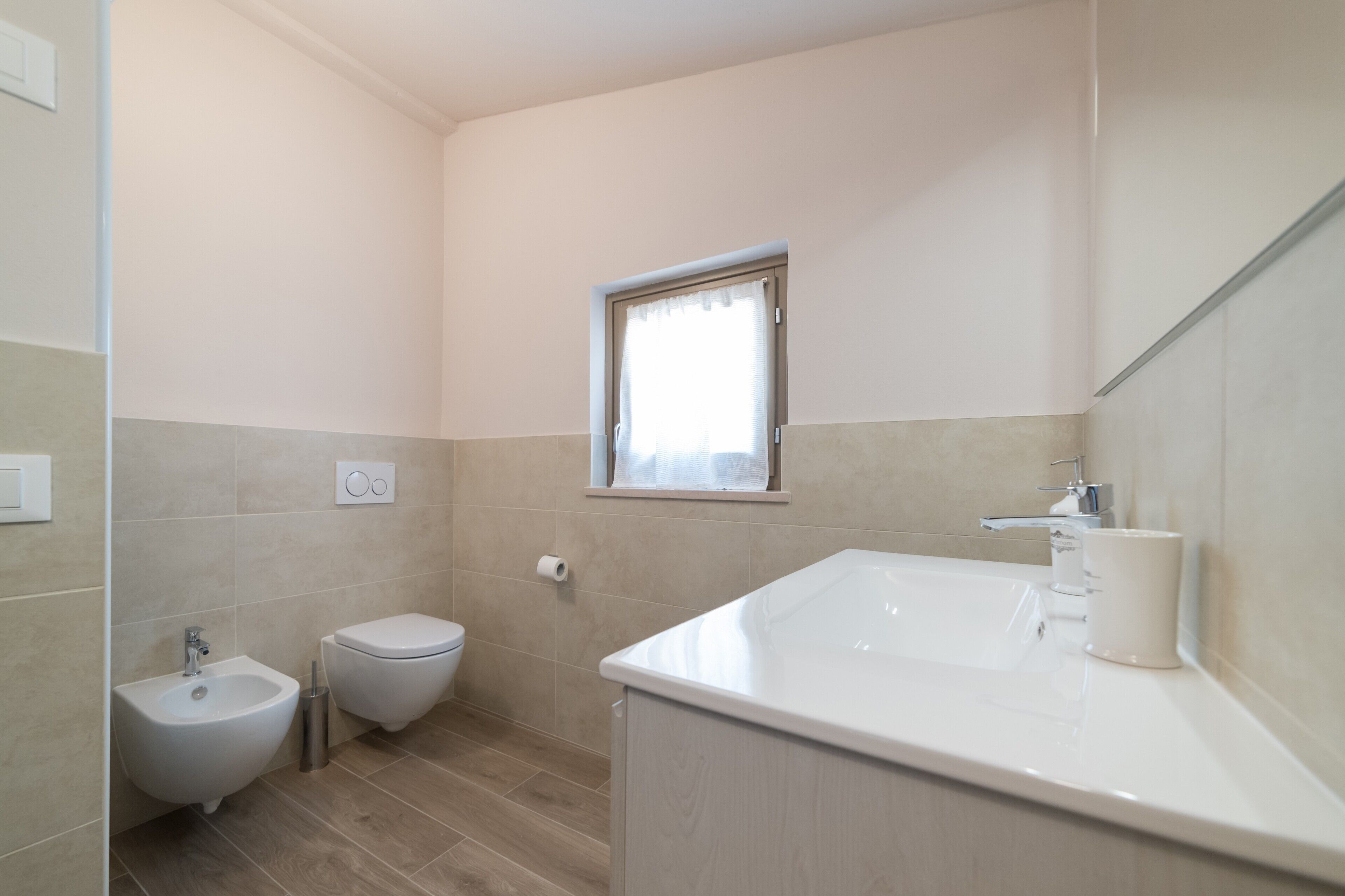 A small, modern bathroom with a bidet, toilet, and a sink with a mirror.