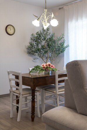 Ein Essbereich mit Holztisch, weißen Stühlen, einer Chandelier-Leuchte, einer Uhr und einem Blumentopf.