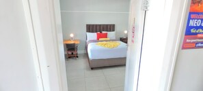 Ein Hotelzimmer mit einem Bett, einem Schreibtisch mit Lampe und einer Tür mit einer Willkommensschild.