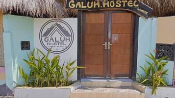 Entrada de un hostal con una puerta de madera y un letrero que dice 'GALUH HOSTEL'.