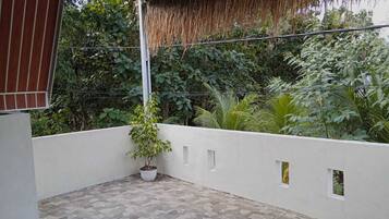 Un espacio exterior cubierto con piso de baldosas, plantas en macetas y una pared blanca con ventanas pequeñas.