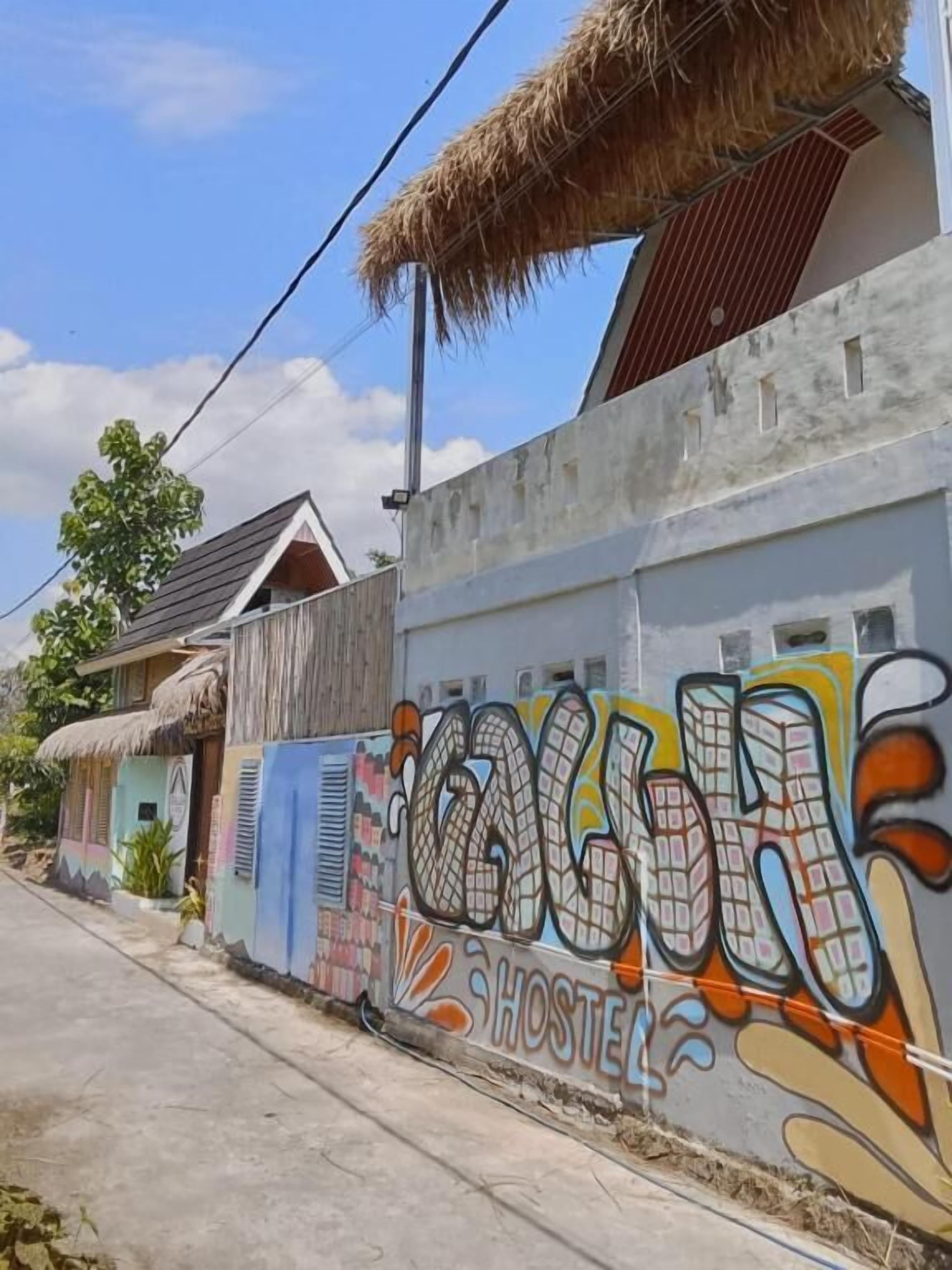 Un hostal con grafitis coloridos en la pared exterior, un techo de paja y un sendero de concreto.