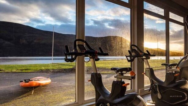 Un espace dédié au vélo d’intérieur, équipé de deux vélos d’appartement et d’un rameur, avec une vue sur un lac et des montagnes grâce à de grandes fenêtres.