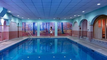 Una piscina con una persona caminando, rodeada de muros decorados con un mural de un bosque.