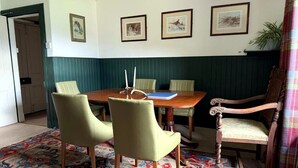 Un coin repas avec une table en bois, quatre chaises, un tapis à motifs et des œuvres d’art encadrées accrochées au mur.