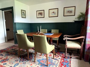 A dining area with a wooden table, four chairs, a patterned rug, and framed artwork on the wall.