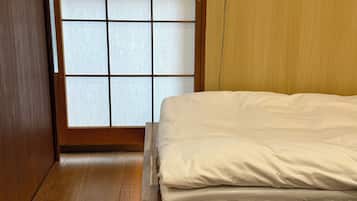 Ein Zimmer mit einem Bett, Holzboden, einer Schiebetür und Blick durch ein fenster mit Gittermuster.