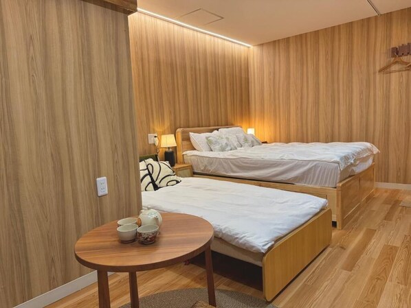 Ein Zimmer mit zwei Holzbett, einem kleinen runden Tisch mit Tassen und einem hängenden Kleiderständer.