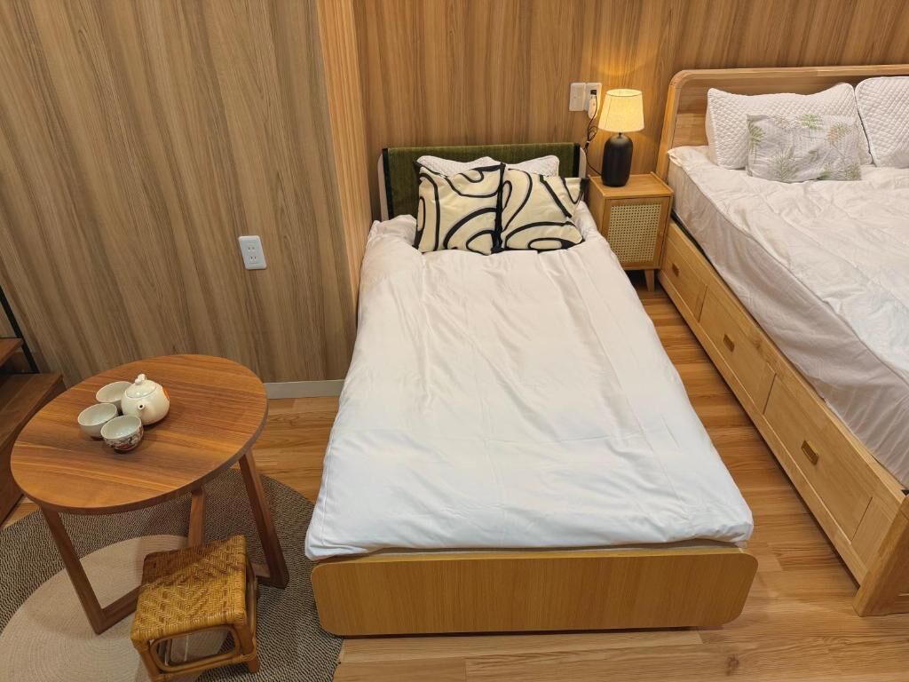 A single bed with a wooden frame, a bedside table with a lamp, and a small round table with teapots.