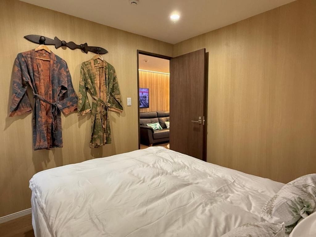 Quarto de hotel com uma cama, uma porta de madeira e um cabide de parede com dois casacos.