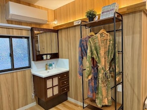 Ein Badezimmer mit einem Holzkosmetikschrank, einem Spiegel, einem Bademantelständer und einem Fenster.