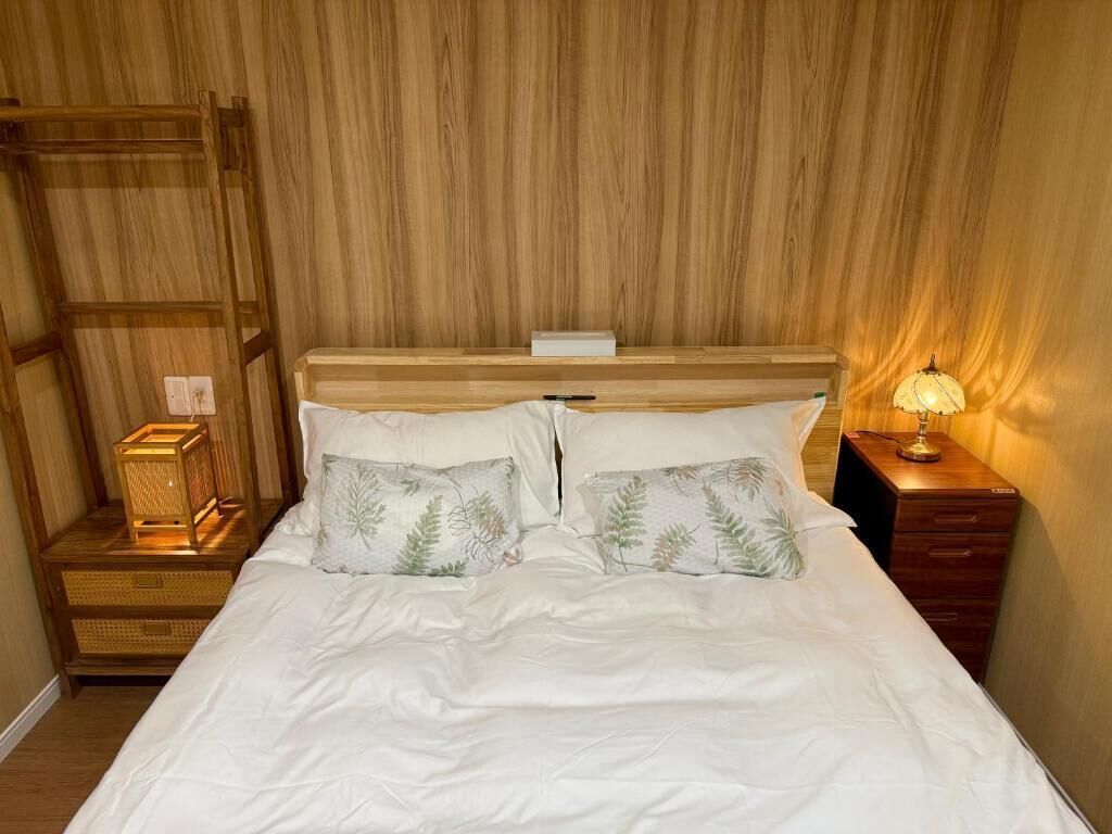 A bed with white bedding and two decorative pillows, a bedside table with a lamp, and a wooden headboard.