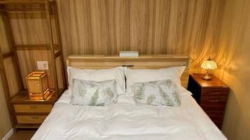 A bed with white bedding and two decorative pillows, a bedside table with a lamp, and a wooden headboard.