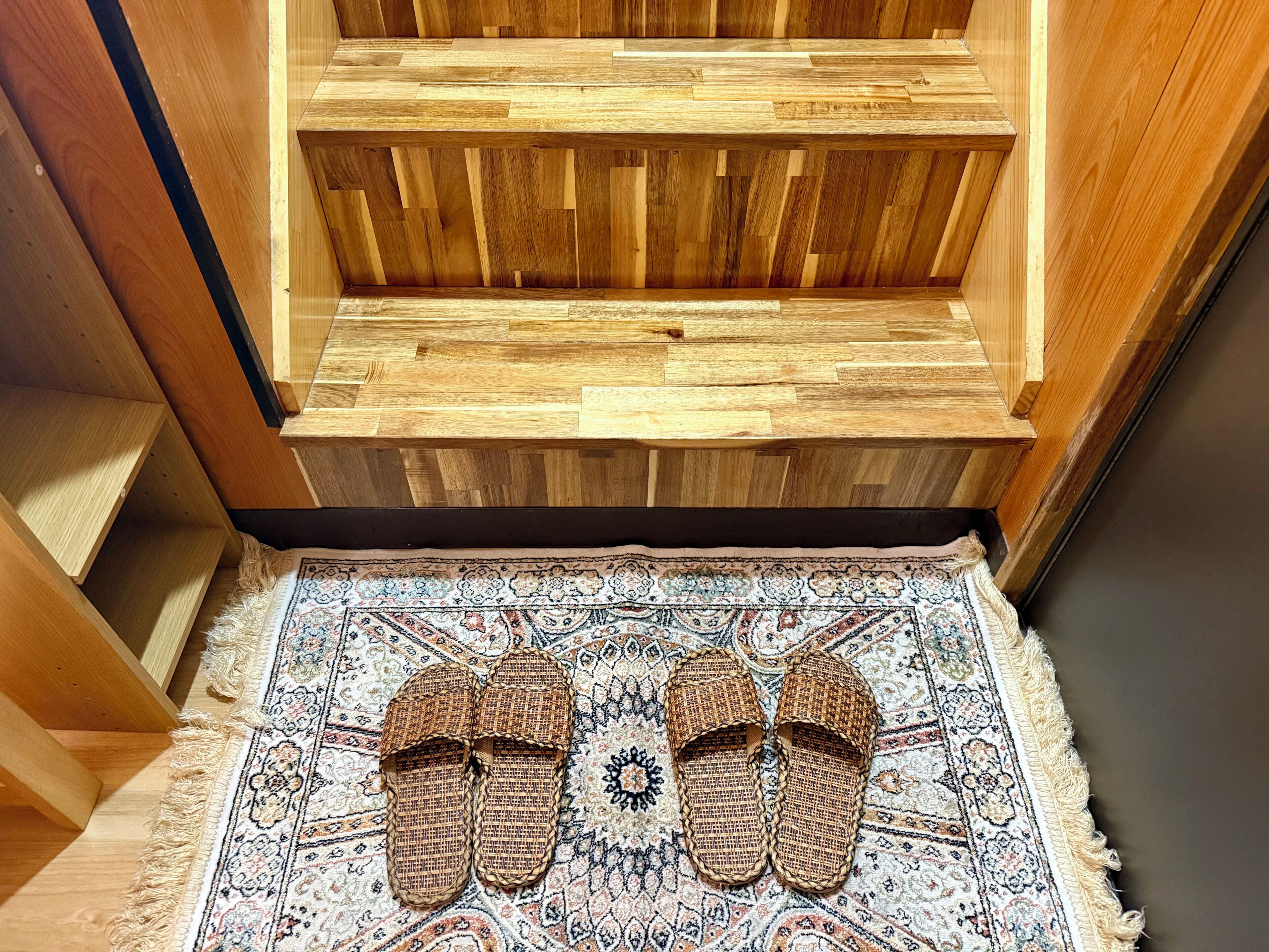 Un banco de madera con un tapete tejido y zapatillas encima.