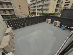 Terraço no telhado com aparelhos de ar condicionado, guarda-corpo de metal e vista dos edifícios ao redor.