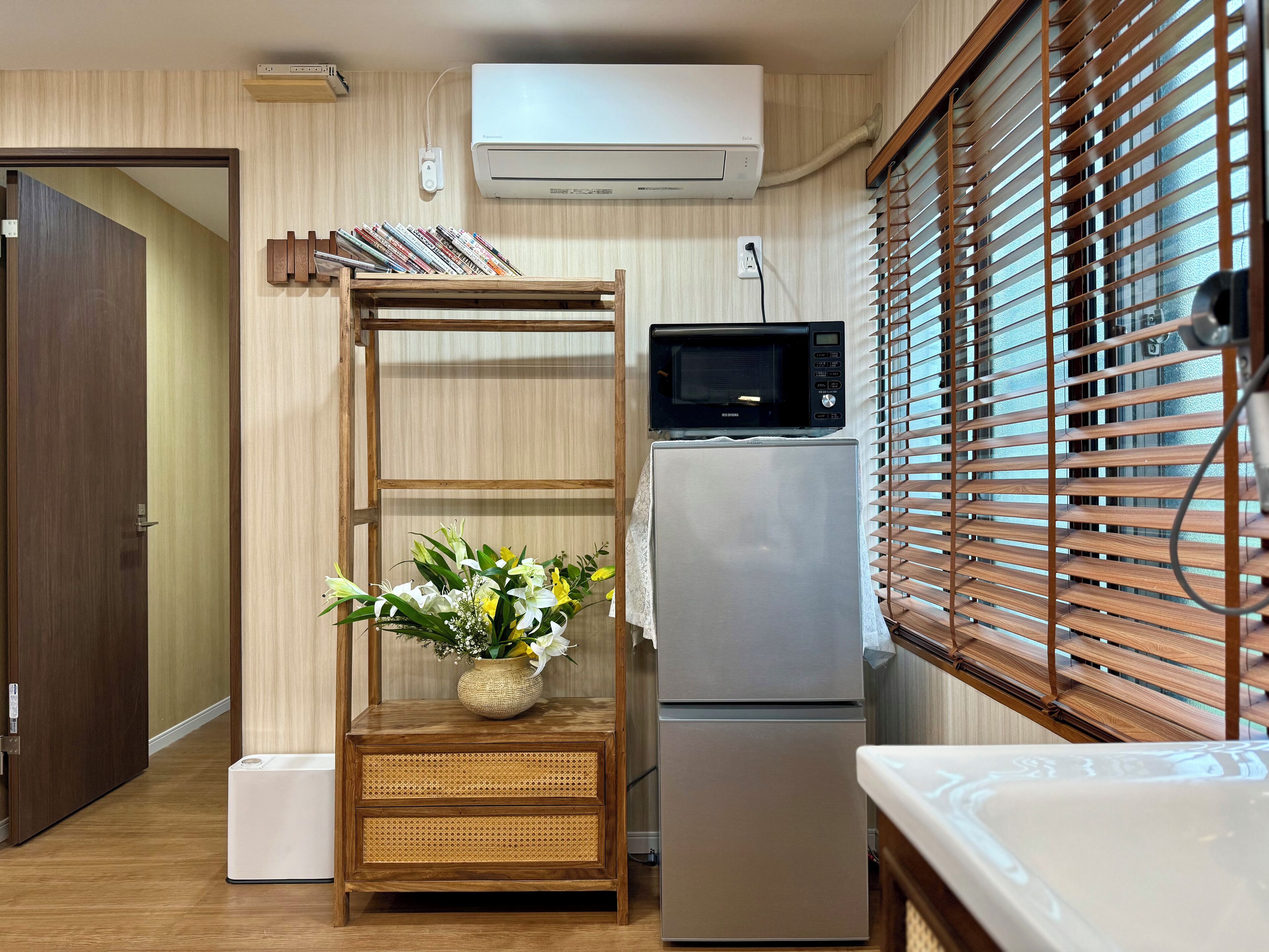 Cocina compacta con refrigerador, microondas y repisa de madera con un jarrón de flores.