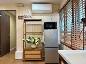 A compact kitchen with a refrigerator, microwave, and a wooden shelf with a vase of flowers. - TOKYO STAR HOUSE (Tokyo)