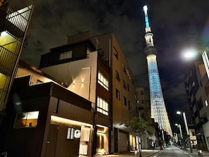 A nighttime cityscape with a prominent illuminated tower, modern buildings, and a street with minimal traffic. - TOKYO STAR HOUSE (Tokyo)