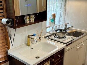A kitchen with a sink, a stove, a mirror, and a shelf with a hairdryer and decorative items. - TOKYO STAR HOUSE (Tokyo)