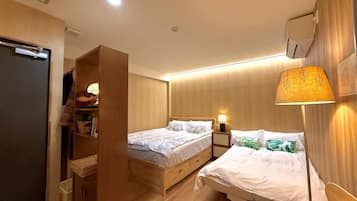 Habitación de hotel con dos camas, un armario, una mesita de noche con lámpara y una pequeña zona de estar.