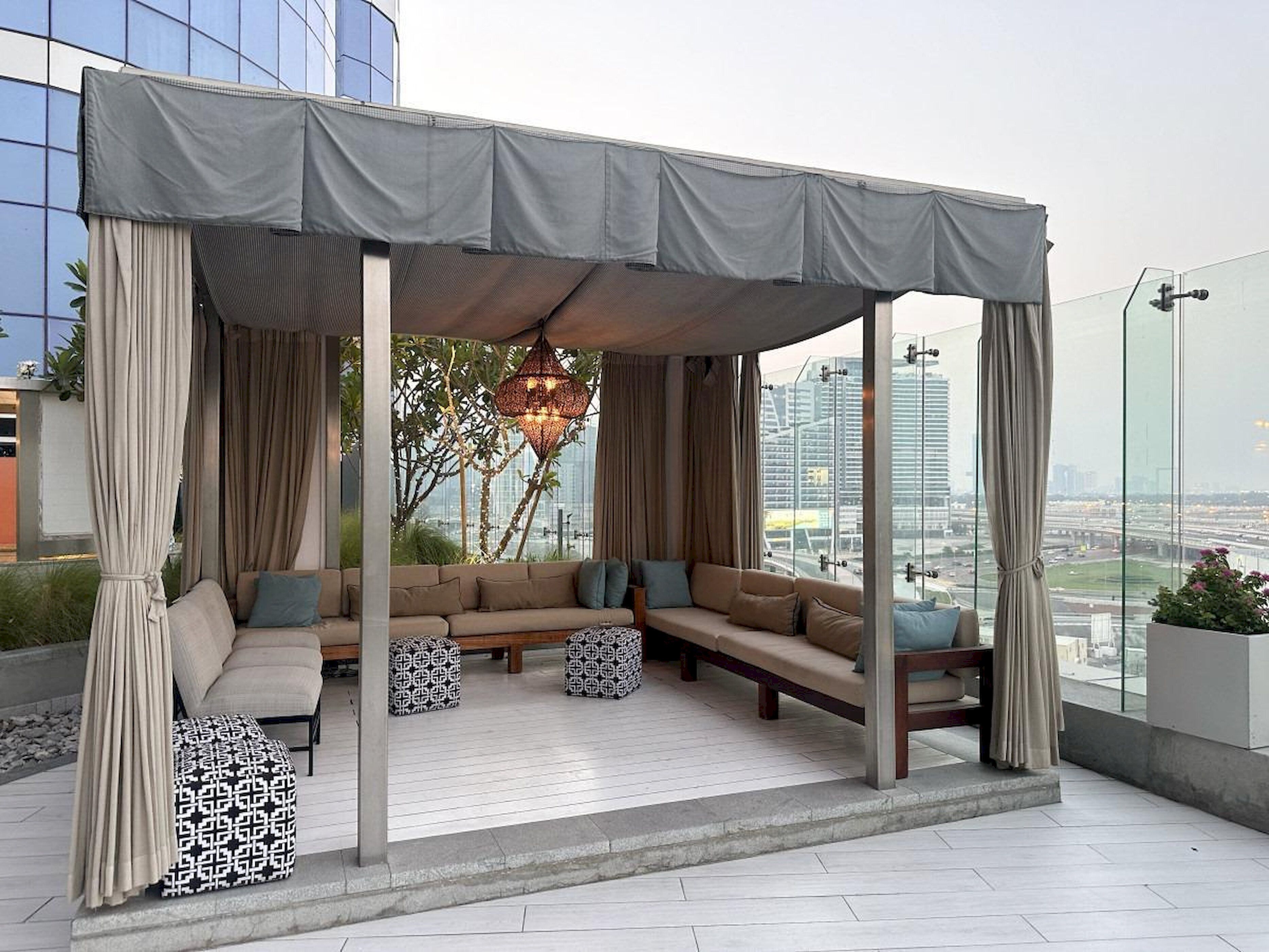 A rooftop lounge with a covered seating area, a patterned ottoman, and a hanging light fixture.