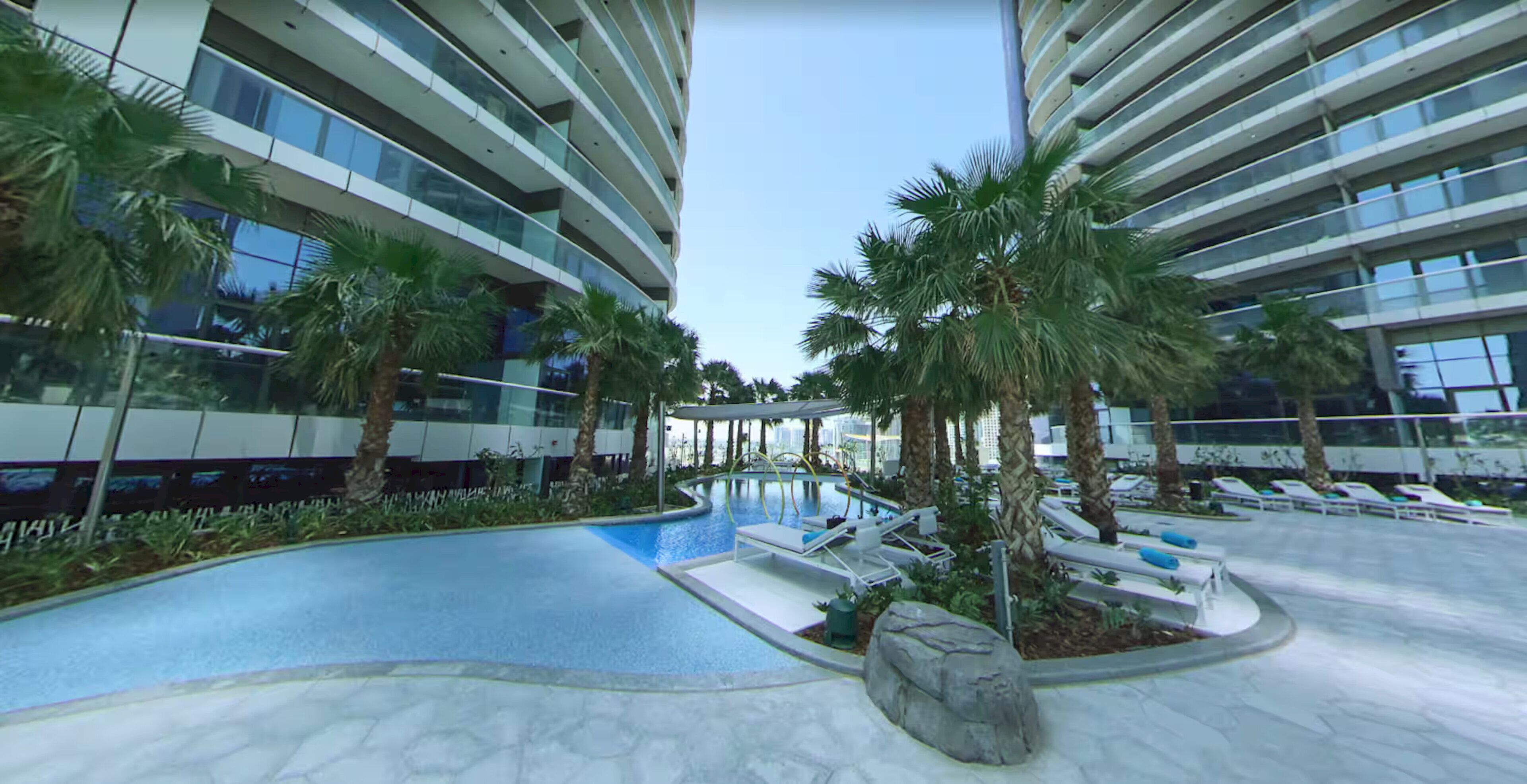 A modern hotel with a swimming pool, palm trees, and lounge chairs.