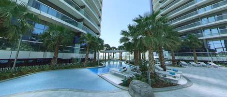 A modern hotel with a swimming pool, palm trees, and lounge chairs.