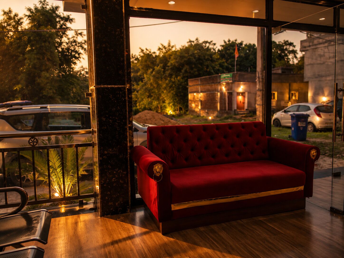 A red sofa in a modern room with a glass door leading to a view of parked cars and trees.