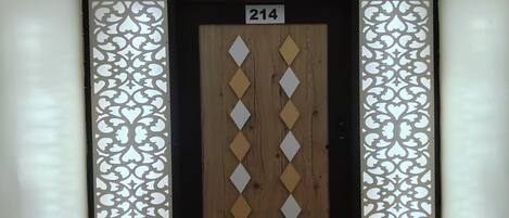 A hotel room entrance with a numbered door, decorative panels, and a wooden door with diamond-shaped cutouts.