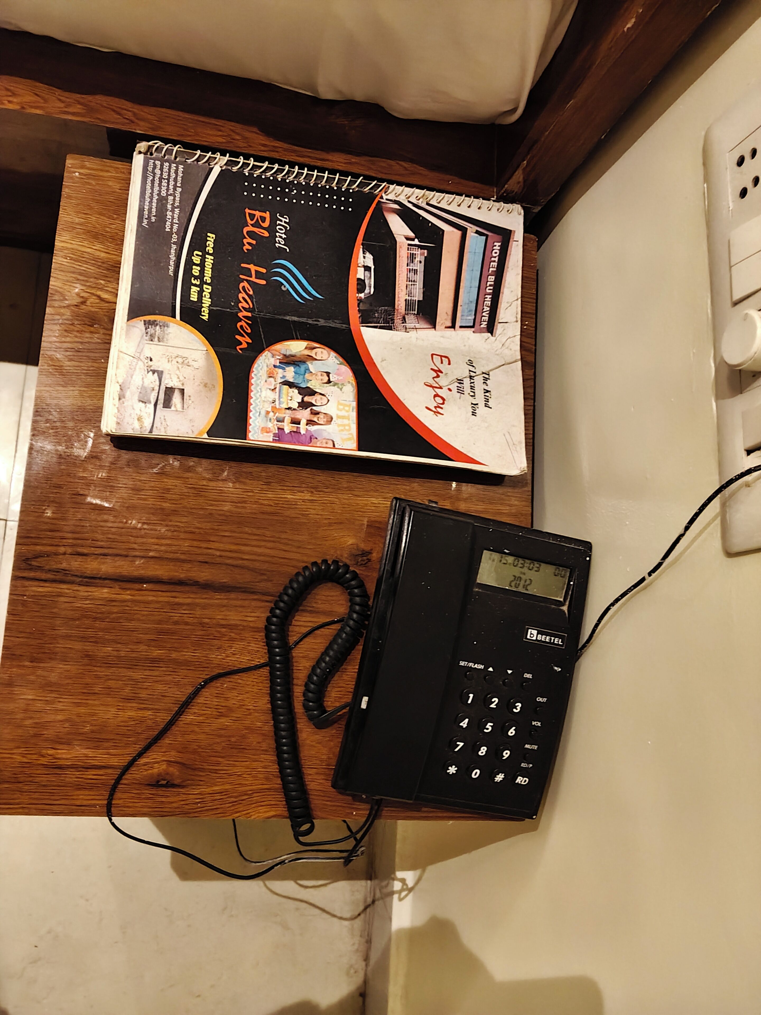 Une brochure d’hôtel et un téléphone noir sur un bureau en bois.
