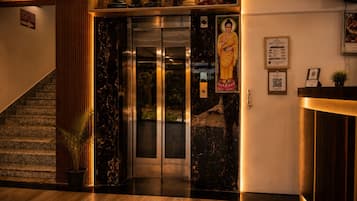 A hotel lobby with a reception desk, a staircase, and a statue of a deity.
