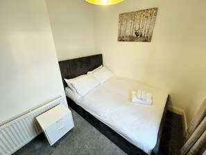 A neatly made bed with white linens, a headboard, and a small bedside table with drawers. - Spacious Home, Parking (Dartford)