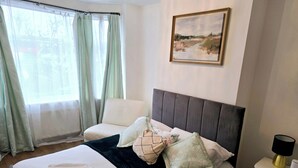 Habitación de hotel con cama, una silla, mesita de noche, lámpara y un cuadro en la pared.