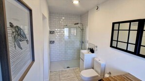 Un baño con cabina de ducha de vidrio, inodoro y una obra de arte enmarcada en la pared.