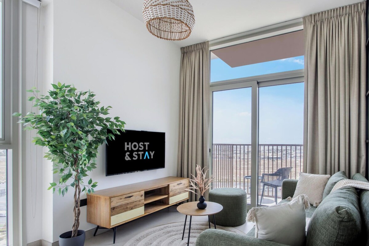 A modern living room with a large window, a flat-screen TV, a wooden console table, a green sofa, and a potted plant.