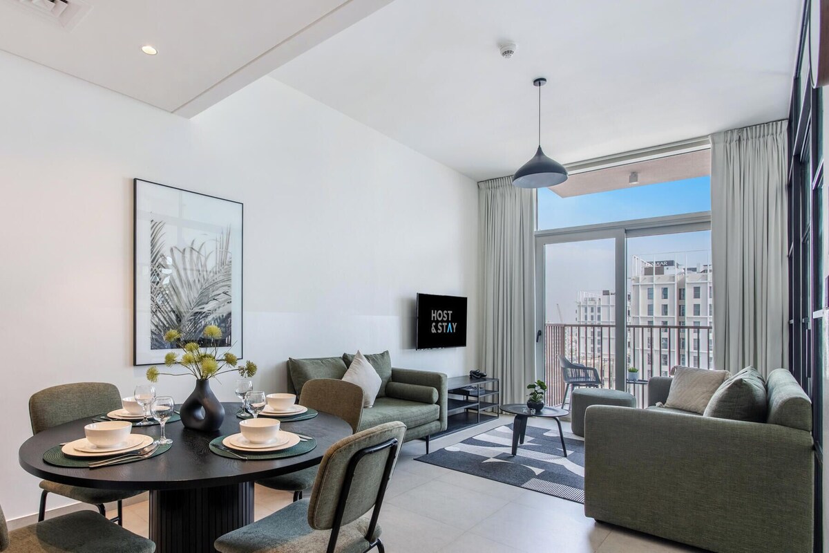 A modern living room with a dining area, a sofa set, a large window with a city view, and a mounted artwork.