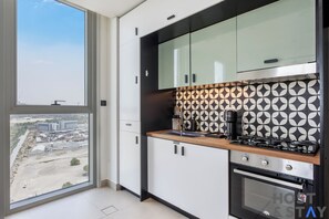 A modern kitchen with a large window, a stove, and a view of an industrial area. - Collective 2.0 Dubai Hills | Host & Stay (Dubai)