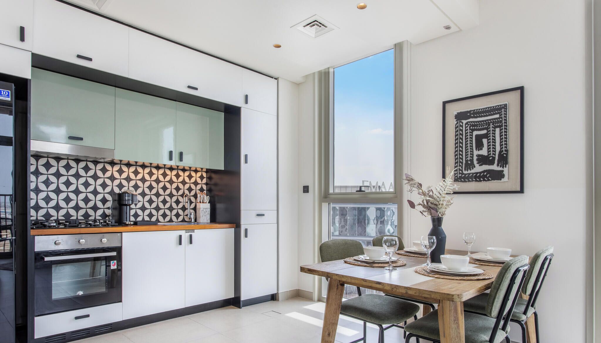 A modern kitchen with a dining area, featuring a large window, a stove, and a tiled backsplash.