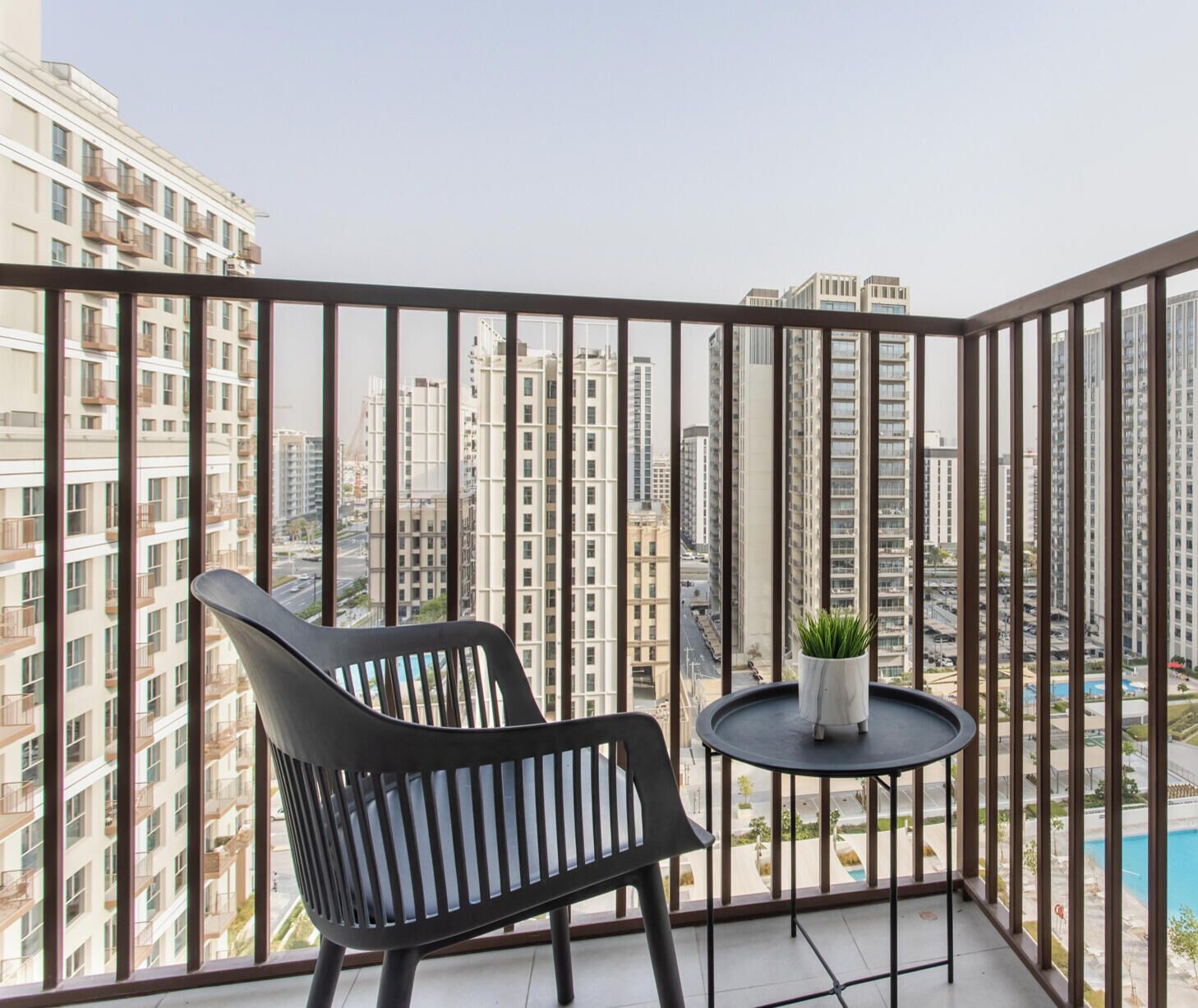 A balcony with a black chair and a small table with a plant.