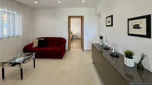 Een moderne woonkamer met een rode bank, een glazen salontafel, een donker houten kast en een ingelijst kunstwerk aan de muur.