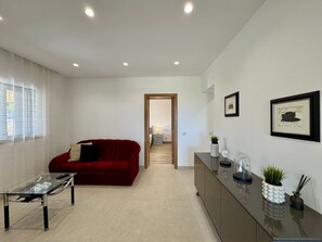 A modern living room with a red sofa, a glass coffee table, a dark wooden cabinet, and a framed picture on the wall. - ALGARVE COUNTRY MODERN VILLA WITH POOL by HOMING (Faro)
