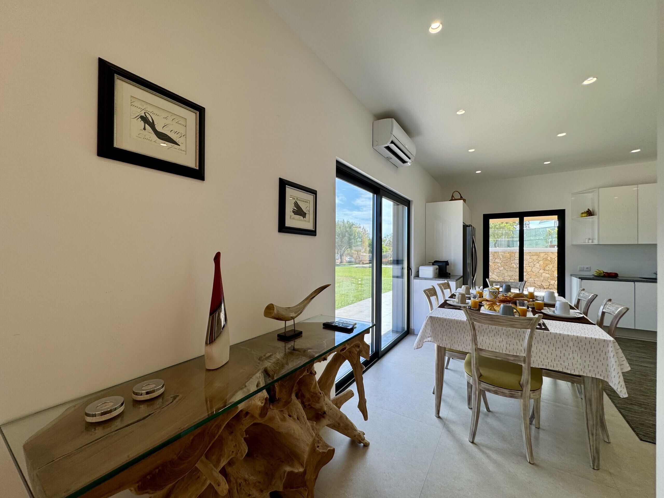 Uma sala de jantar com mesa de vidro, cadeiras e vista para o exterior.