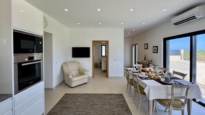 Een moderne keuken met inbouwapparatuur, een eethoek met een tafel voor vier personen, en uitzicht op zee door grote ramen.