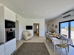 A modern kitchen with built-in appliances, a dining area with a table set for four, and a view of the sea through large windows. - ALGARVE COUNTRY MODERN VILLA WITH POOL by HOMING (Faro)