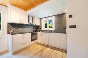 A modern kitchen with white cabinets, a black countertop, and a wooden ceiling. - Géroux- Modern Apt | Quiet | Mountain View | Garden (Chamonix-Mont-Blanc)